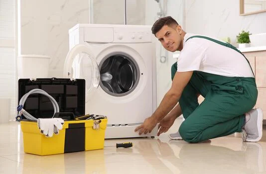 Technician kneeling at a washing machine with a yellow toolbox beside him