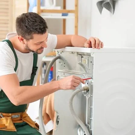 Technician in green overalls inspecting the rear panel of a washing machine